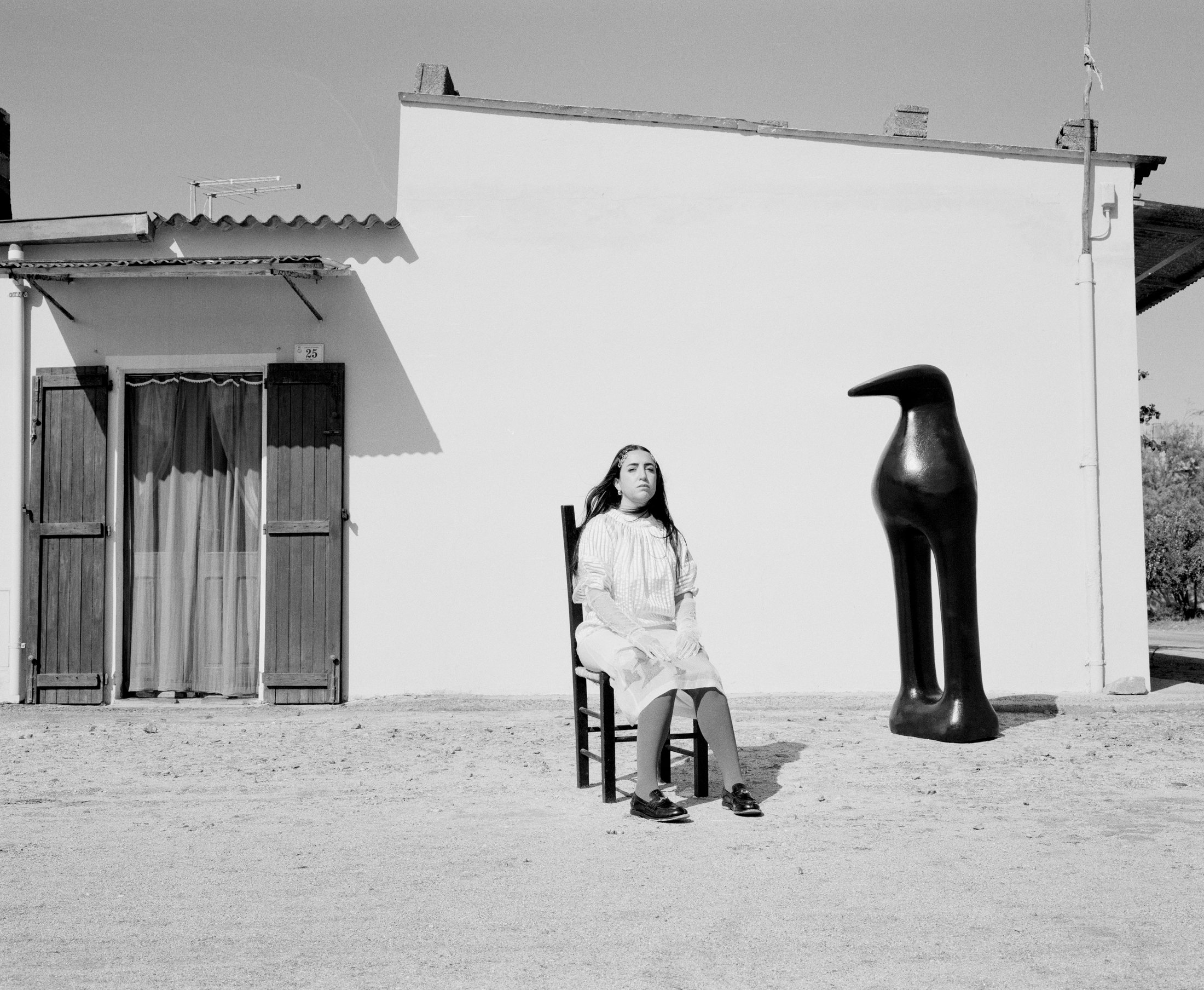 Black and white portrait of BLUEM seated beside a dark crow sculpture.