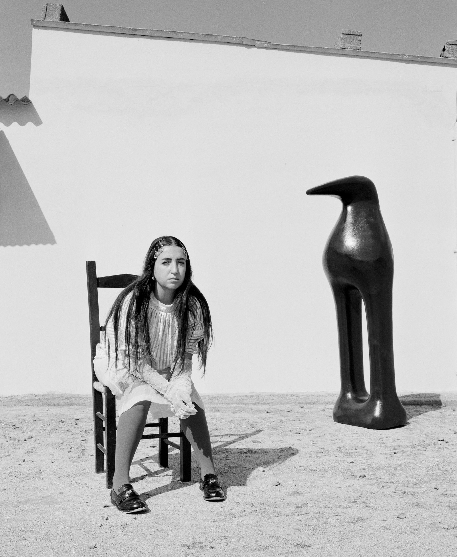 Black and white portrait of BLUEM seated beside a sculpture.